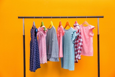 Rack with stylish child clothes on color background