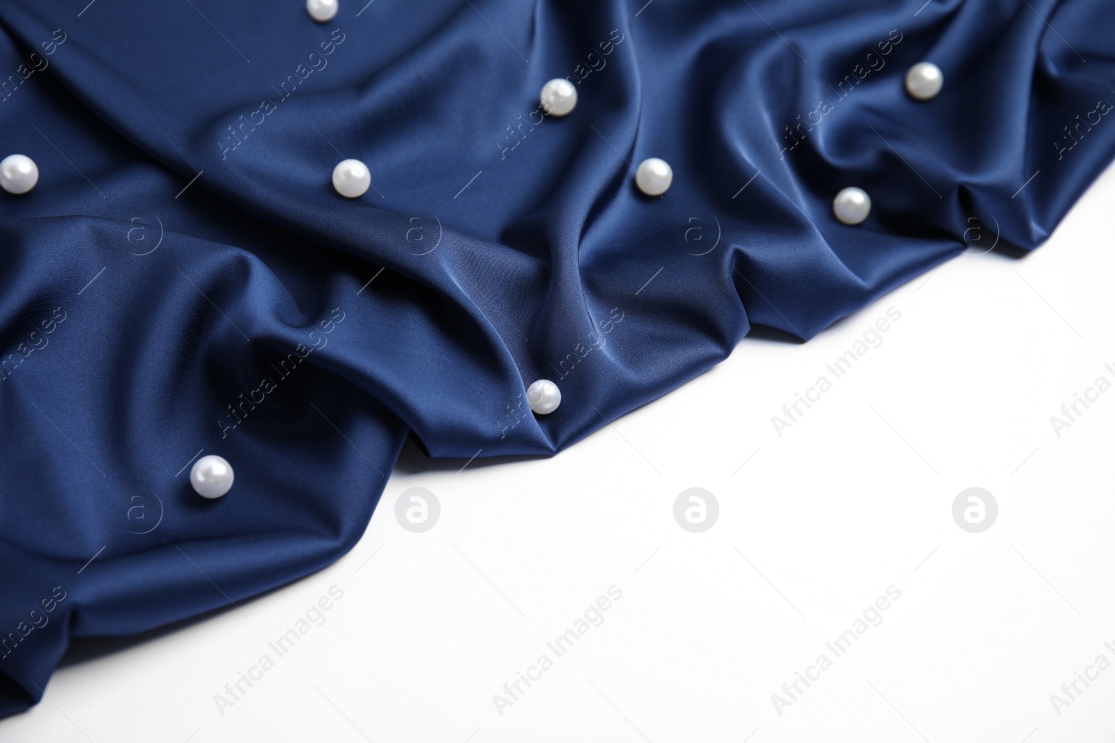 Photo of Texture of delicate dark blue silk with pearls on white background