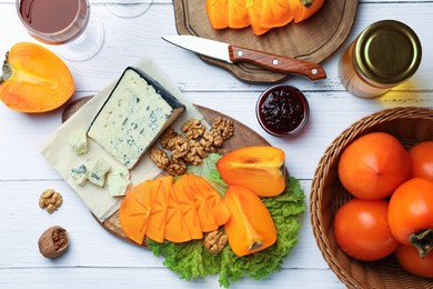 Delicious persimmon, blue cheese and nuts served on white wooden table, flat lay
