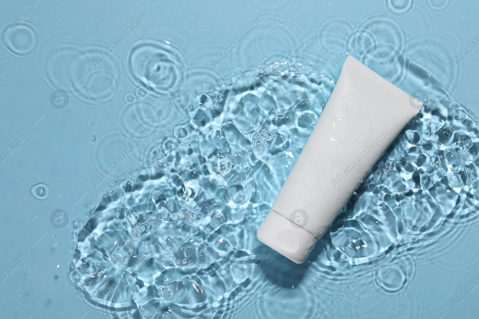 Photo of Tube of face cleansing product in water against light blue background, top view. Space for text