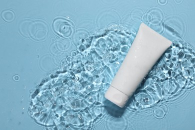 Tube of face cleansing product in water against light blue background, top view. Space for text