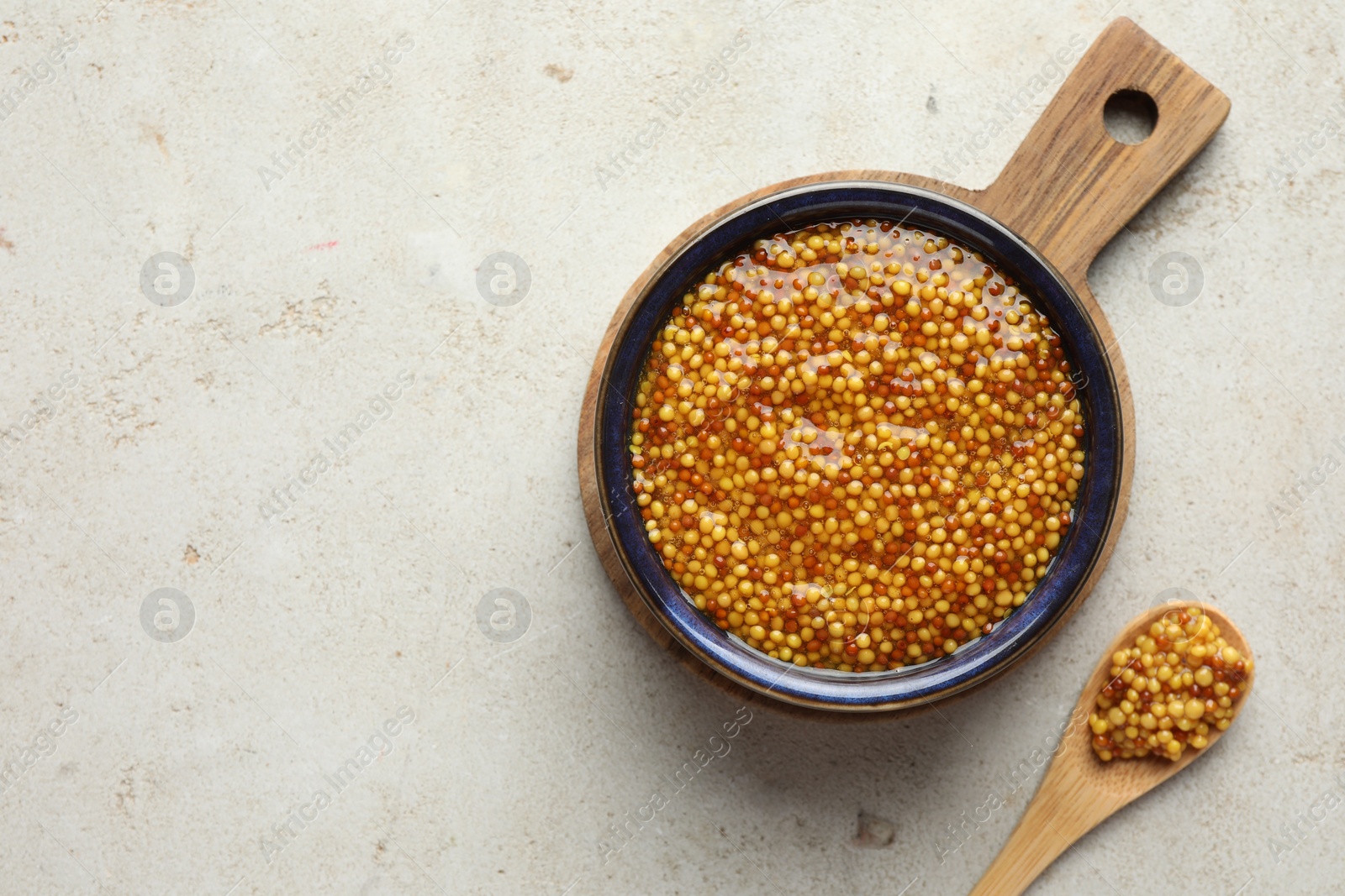 Photo of Bowl and spoon with whole grain mustard on light table, top view. Space for text