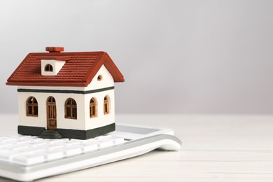 Photo of Mortgage concept. Model house and calculator on white wooden table against light grey background, space for text