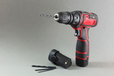 Electric screwdriver, drill bits and battery on grey background. Space for text