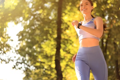 Photo of Attractive sporty woman jogging in beautiful park on sunny day, low angle view. Space for text