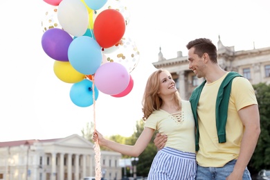 Young couple with colorful balloons outdoors on sunny day