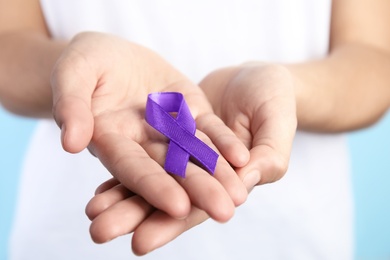 Photo of Woman holding purple ribbon on blue background, closeup. Domestic violence awareness