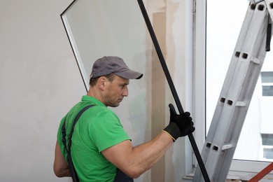 Worker in uniform installing double glazing window indoors