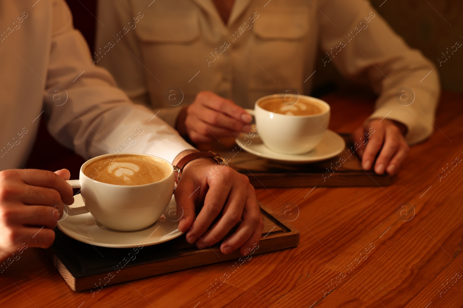 Photo of Couple with cups of aromatic coffee at wooden table, closeup