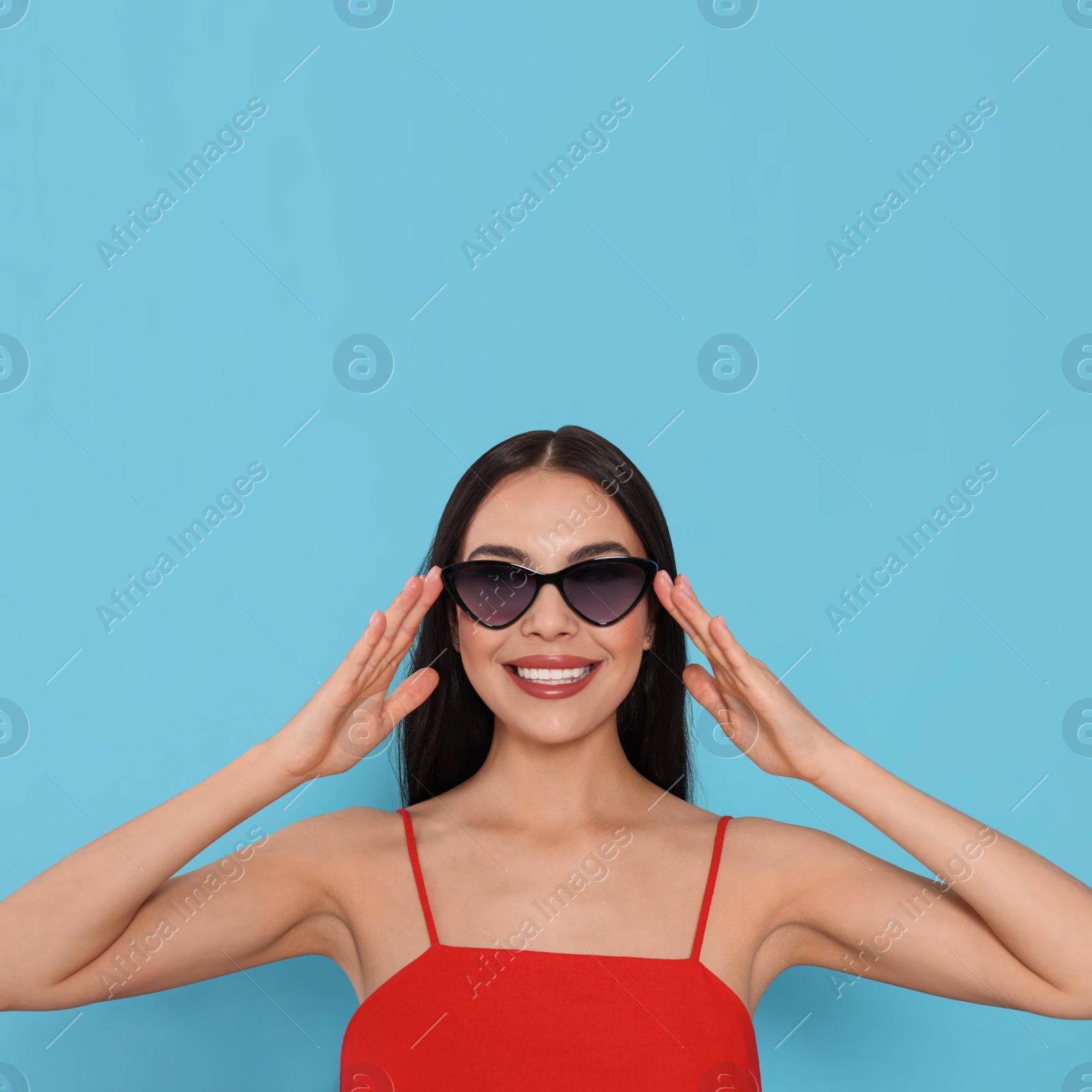 Photo of Attractive happy woman touching fashionable sunglasses against light blue background