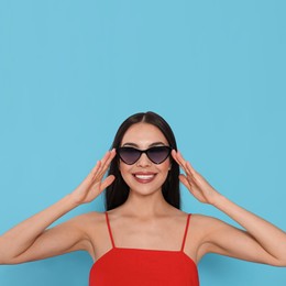 Photo of Attractive happy woman touching fashionable sunglasses against light blue background
