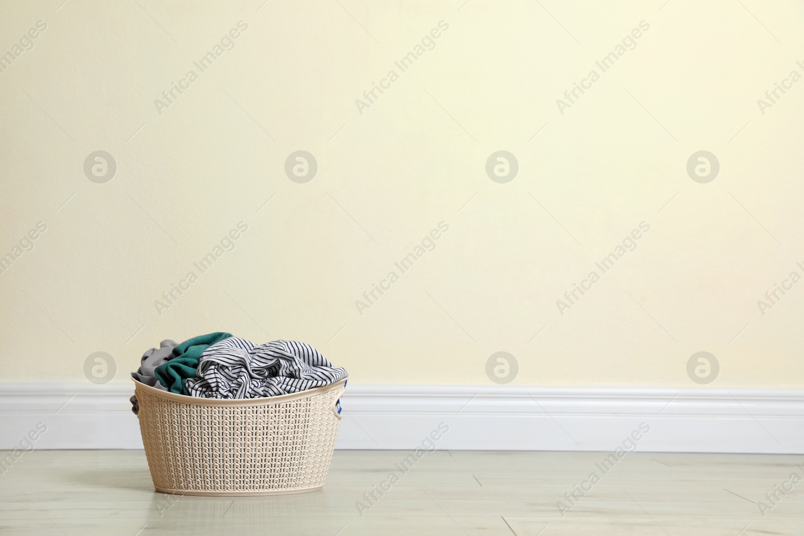 Photo of Plastic laundry basket full of dirty clothes on floor near color wall. Space for text