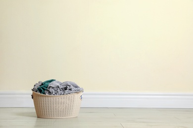 Plastic laundry basket full of dirty clothes on floor near color wall. Space for text