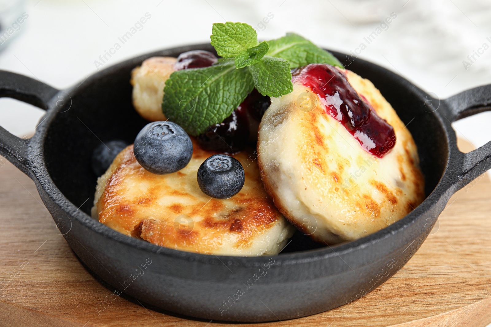 Photo of Delicious cottage cheese pancakes with blueberries, mint and jam in pan