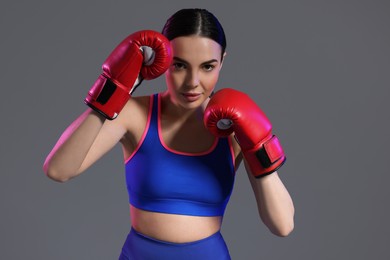 Portrait of beautiful woman wearing boxing gloves in color lights on grey background