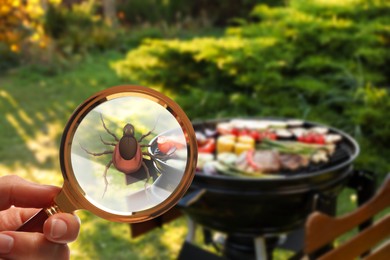 Seasonal hazard of outdoor recreation. Barbecue grill with food and woman showing tick with magnifying glass, selective focus