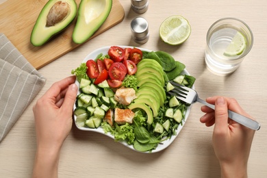 Photo of Woman eating delicious avocado salad with fried chicken at wooden table, top view