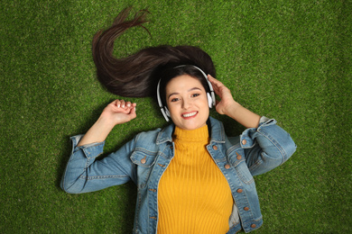 Young woman listening to audiobook while lying on grass, top view