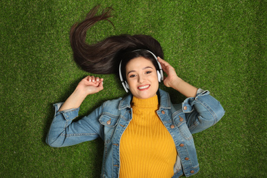 Photo of Young woman listening to audiobook while lying on grass, top view