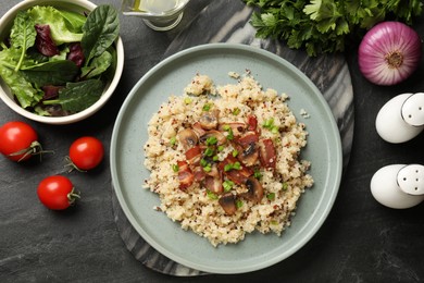 Photo of Plate of tasty quinoa porridge with fried bacon, mushrooms and vegetables on black table, flat lay