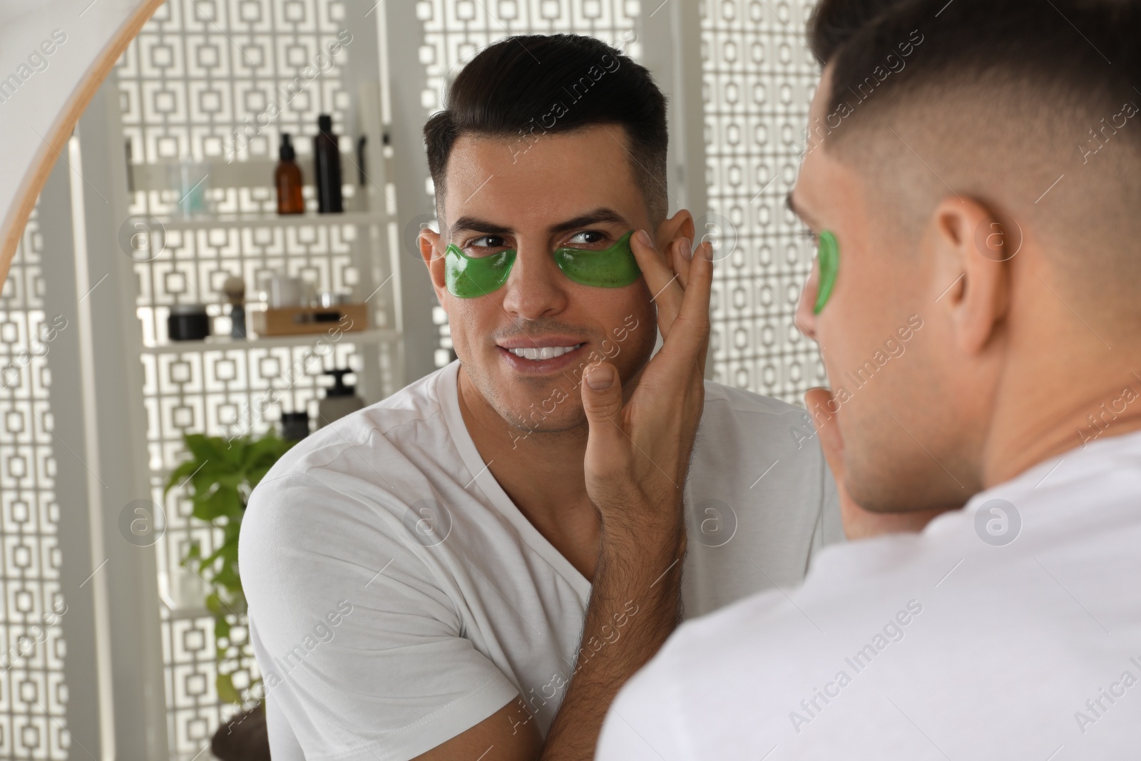 Photo of Man applying green under eye patch near mirror at home