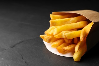 Photo of Paper bag with tasty french fries on black table, closeup. Space for text