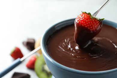 Photo of Dipping strawberry into fondue pot with chocolate, closeup