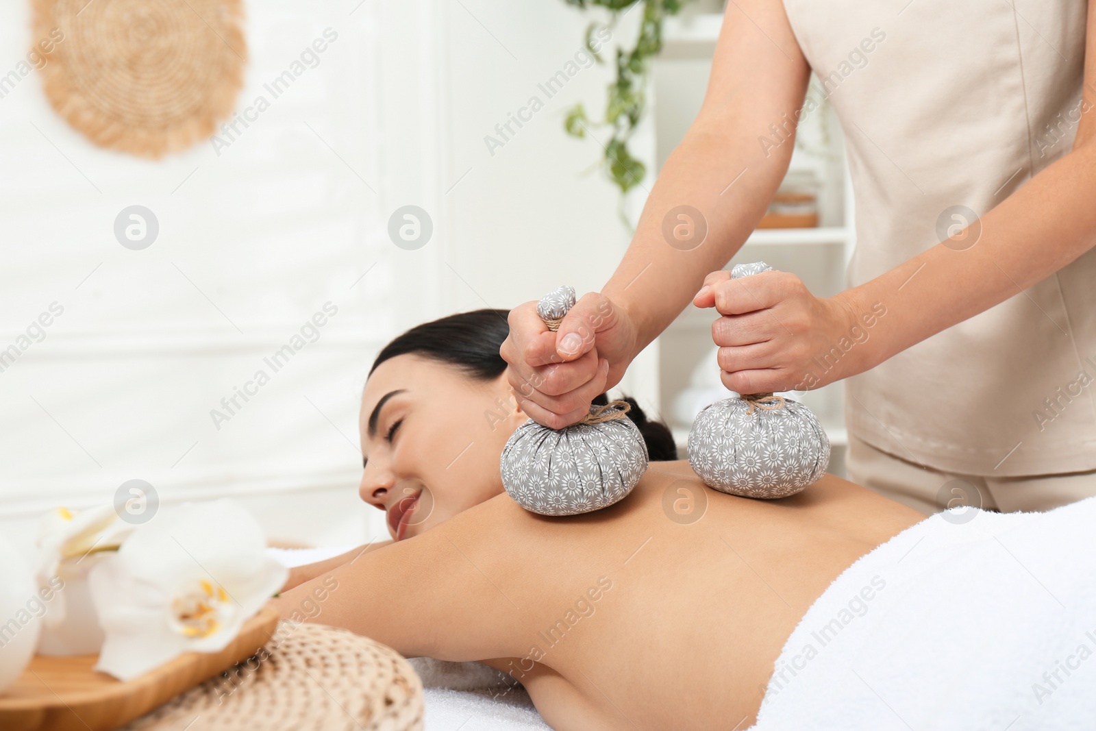 Photo of Young woman receiving herbal bag massage in spa salon