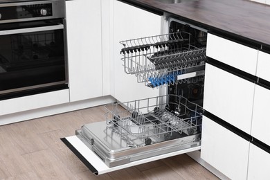 Photo of Open clean empty dishwasher in kitchen. Home appliance