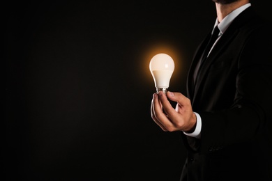 Photo of Businessman holding lamp bulb against dark background, closeup. Space for text