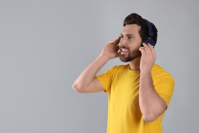 Photo of Happy man listening music with headphones on light grey background. Space for text