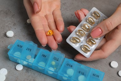 Photo of Woman taking pills from plastic box at grey table, closeup