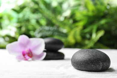 Dark stones and beautiful flower on sand against blurred green background. Zen, meditation, harmony