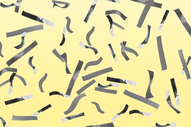 Shiny silver confetti falling on light yellow background