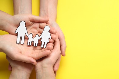 People holding paper family cutout on yellow background, top view. Space for text