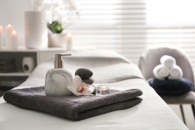 Dispenser, candle and orchid flower on couch in spa salon