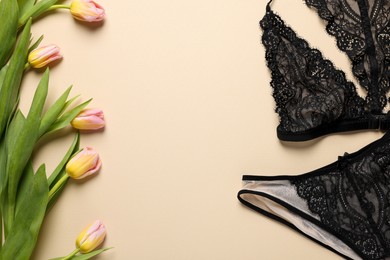 Photo of Elegant black women's underwear and beautiful tulips on beige background, flat lay. Space for text