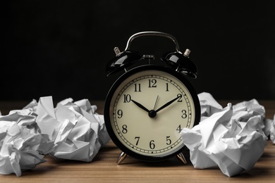 Crumpled paper balls and alarm clock on wooden table