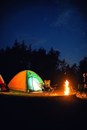 Photo of Glowing camping tent near bonfire in wilderness at night