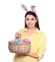 Photo of Beautiful woman in bunny ears headband holding basket with Easter eggs on white background