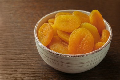 Photo of Bowl of tasty apricots on wooden table. Dried fruits