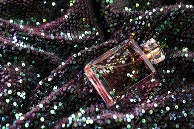 Photo of Luxury perfume in bottle on fabric with colorful sequins, above view