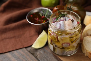 Tasty marinated fish with onion and rosemary in jar on wooden table, closeup