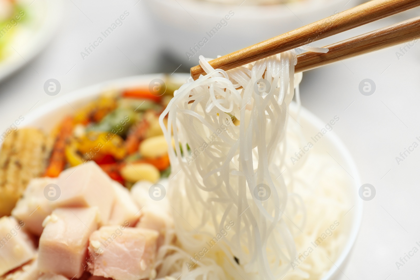 Photo of Chopsticks with tasty cooked rice noodles over bowl, closeup