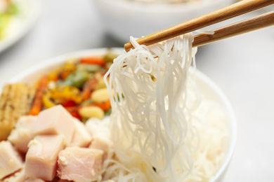 Photo of Chopsticks with tasty cooked rice noodles over bowl, closeup
