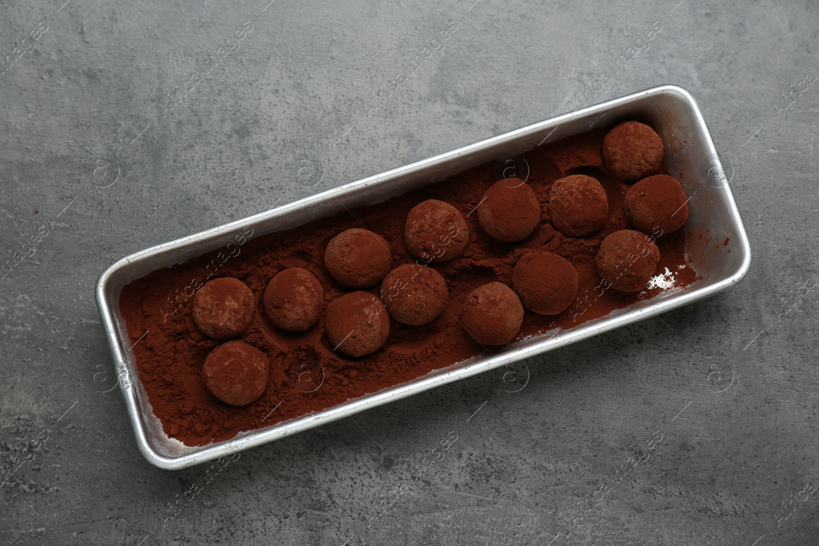 Photo of Delicious chocolate candies powdered with cocoa on grey table, top view