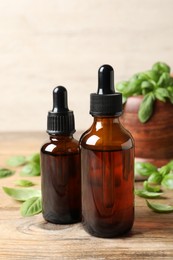 Photo of Bottles of basil essential oil and green leaves on wooden table