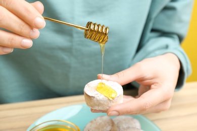 Photo of Woman pouring honey onto cookie at wooden table, closeup