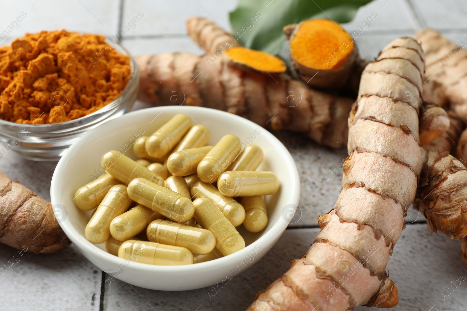 Photo of Turmeric roots, pills and powder on light tiled table, closeup