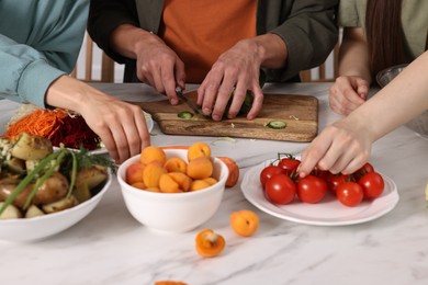 Photo of Friends cooking healthy vegetarian meal at white marble table in kitchen, closeup